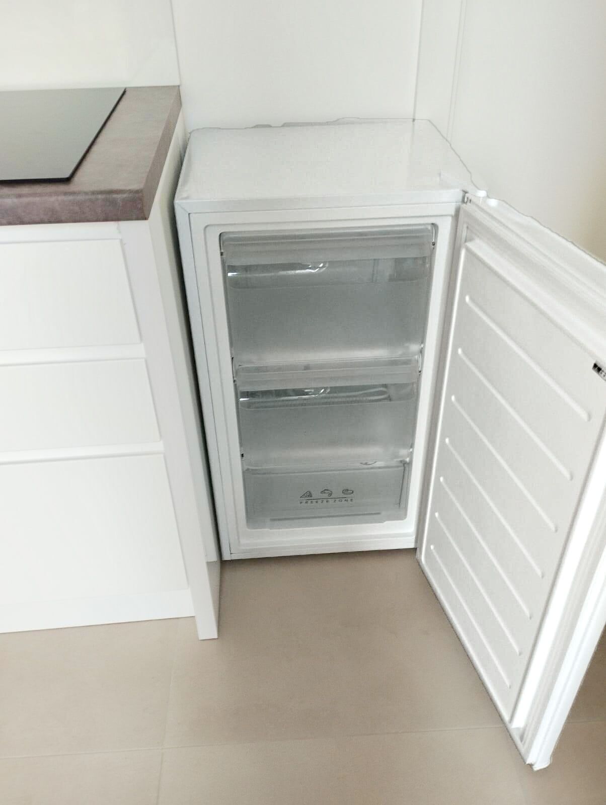 A compact refrigerator with a freezer compartment, located in a small kitchen area with white cabinetry.