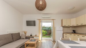 Ein modernes, gut beleuchtetes Wohnzimmer mit einer Couch, einem Couchtisch und einem Fernseher. Es gibt eine Küchenzeile mit Schränken und einem Kühlschrank.