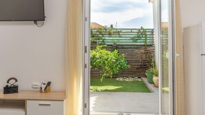 Ein Zimmer mit einer Schiebetür zu einem Balkon, der einen grünen Rasen, Blumentöpfe und einen Holzzaun bietet.