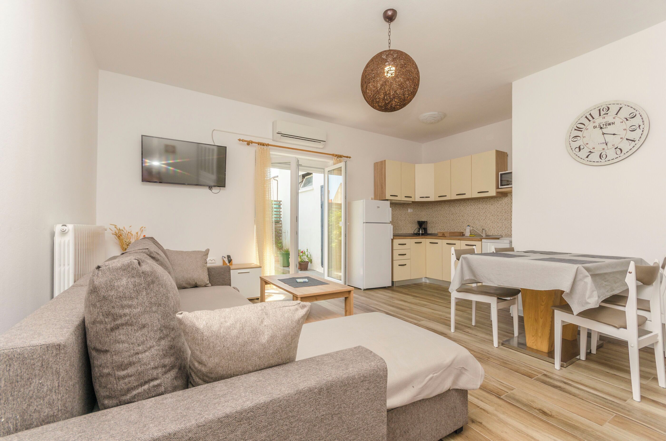A modern living room with a sofa, a dining table, and a kitchen area with cabinets and a refrigerator.