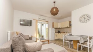 Ein modernes Wohnzimmer mit Sofa, Esstisch und Küchenzeile mit Schränken und Kühlschrank.
