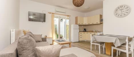 A modern living room with a sofa, a dining table, and a kitchen area with cabinets and a refrigerator.