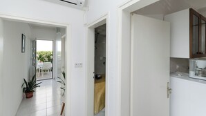 A hallway with a white air conditioner, a potted plant, and a door leading to a room with a bed and a window. - Apartment Nikola (Rab)