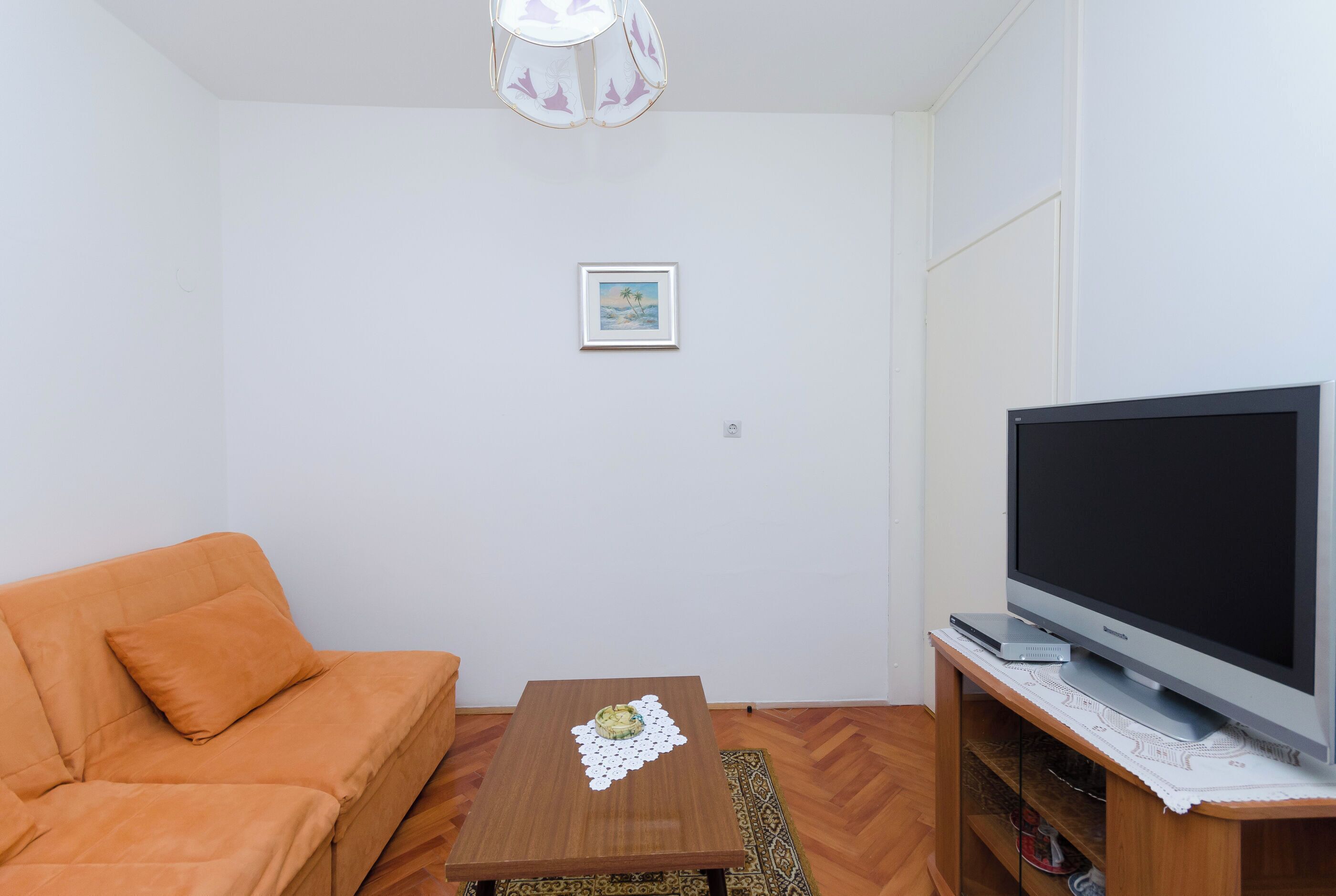 A living room with a sofa, a coffee table with a decorative item, a flat-screen TV on a wooden stand, and a framed picture on the wall.