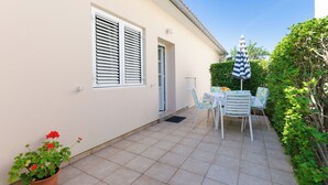 A patio with a table and chairs, a potted plant, and a striped umbrella. - Apartment Nikola (Rab)