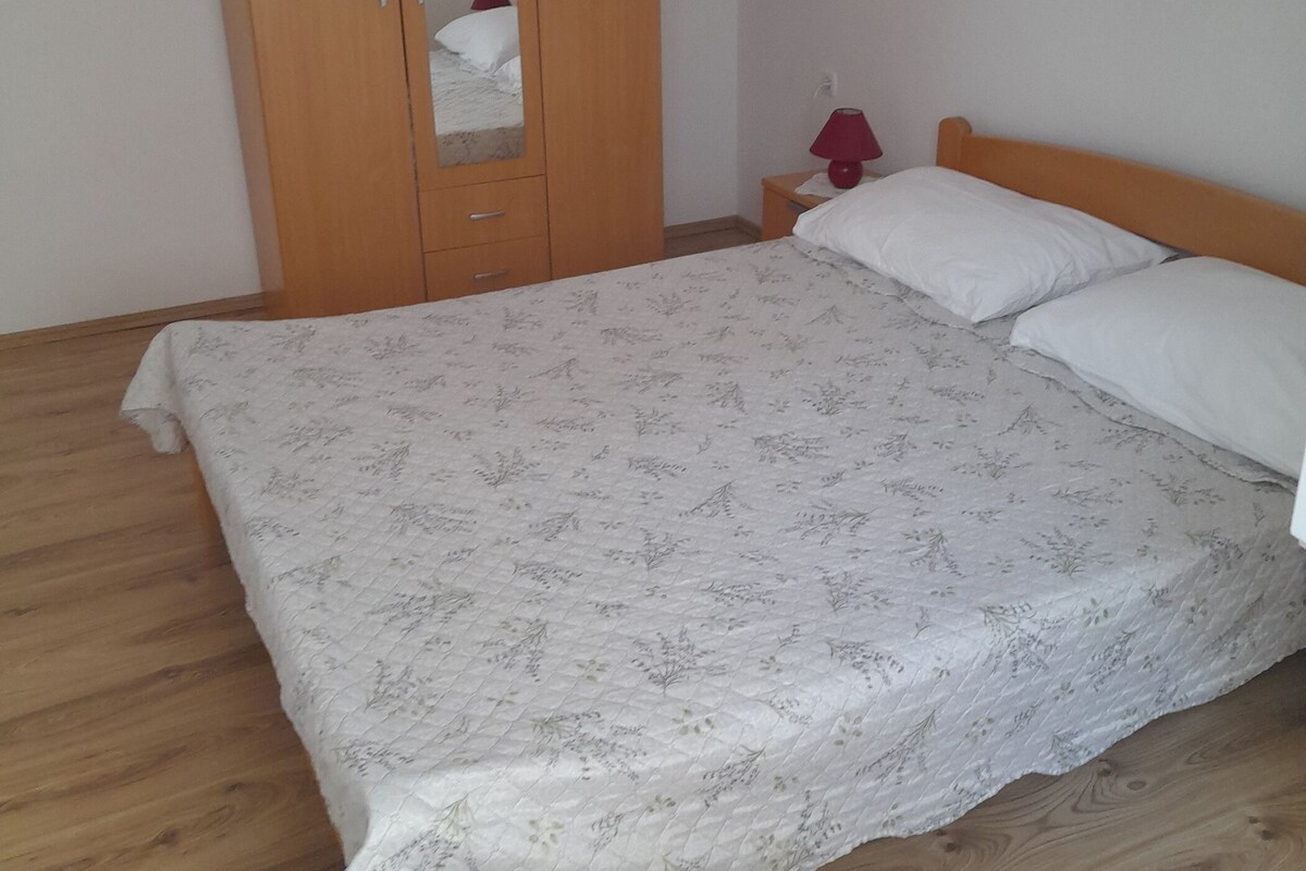 Quarto com armário de madeira, cama com colcha florida e mesa de cabeceira com abajur.