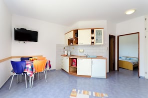 A compact kitchen with a dining area, a TV mounted on the wall, and a bed in the adjacent room. - Apartments Ruzica M (Lopar)