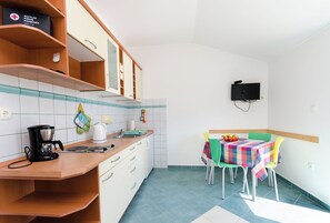 A compact kitchen with a coffee maker, a kettle, and a microwave. There is a dining table with a colorful tablecloth and chairs. - Apartments Ruzica M (Lopar)