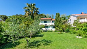 Ένα διώροφο σπίτι με κόκκινη στέγη, περιτριγυρισμένο από πλούσια βλάστηση και έναν καλά περιποιημένο κήπο.