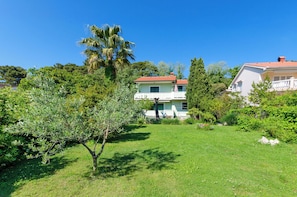 A two-story house with a red roof, surrounded by lush greenery and a well-maintained lawn. - Apartments Ruzica M (Lopar)