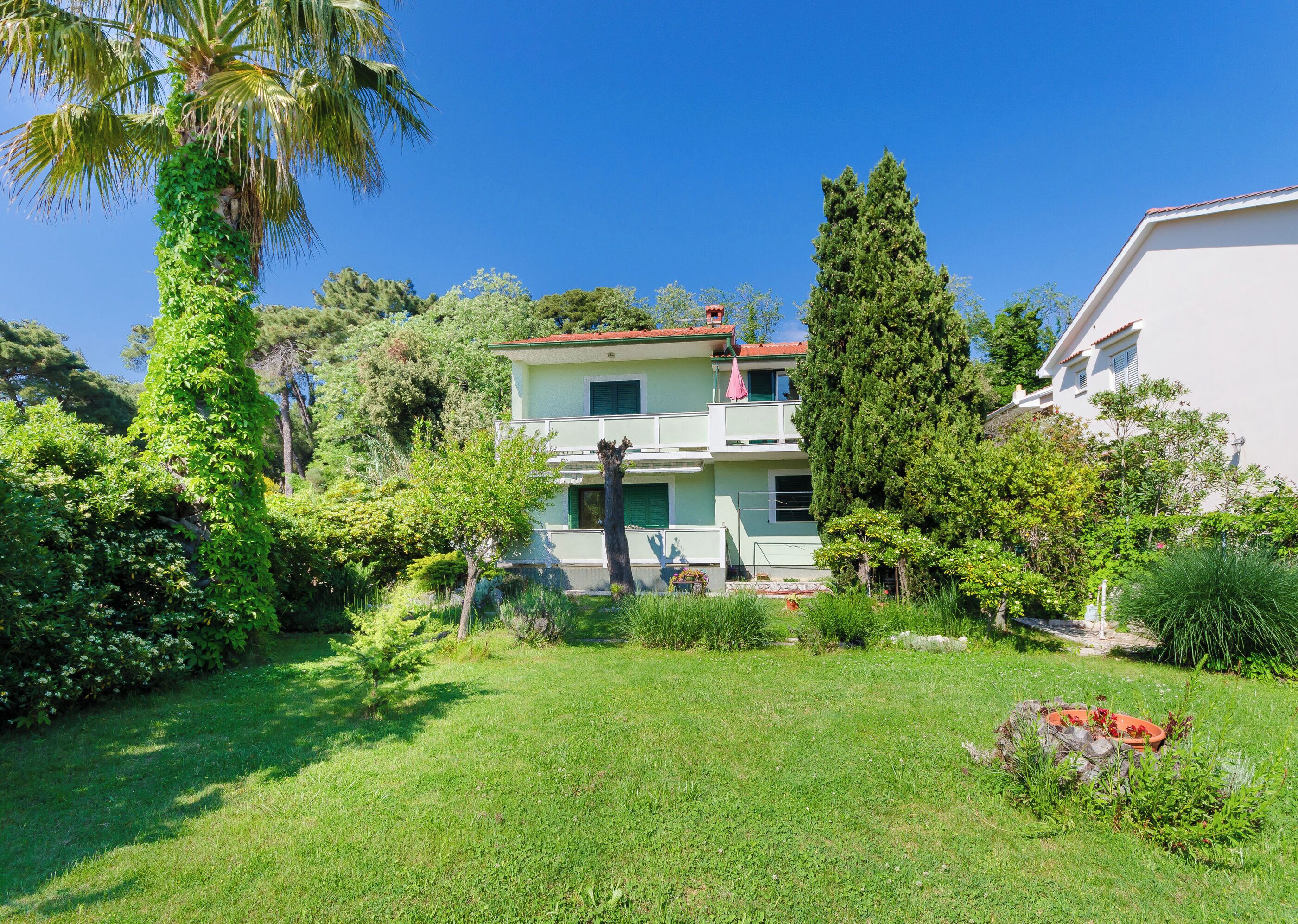 A two-story house with a balcony, surrounded by lush greenery and a well-maintained lawn.