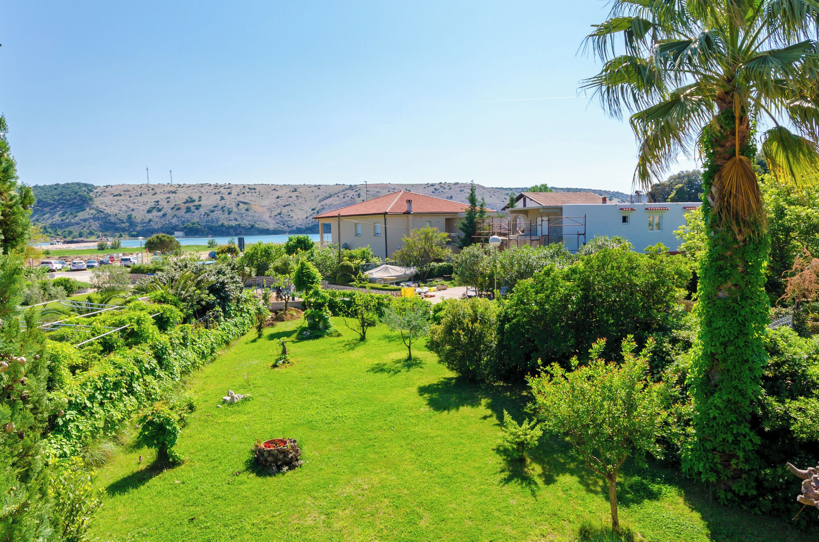 A residential area with a large house, lush greenery, and a view of a body of water and hills in the background.