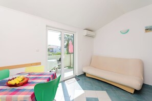 A room with a sofa, a table with a fruit bowl, and a sliding glass door leading to an outdoor area. - Apartments Ruzica M (Lopar)