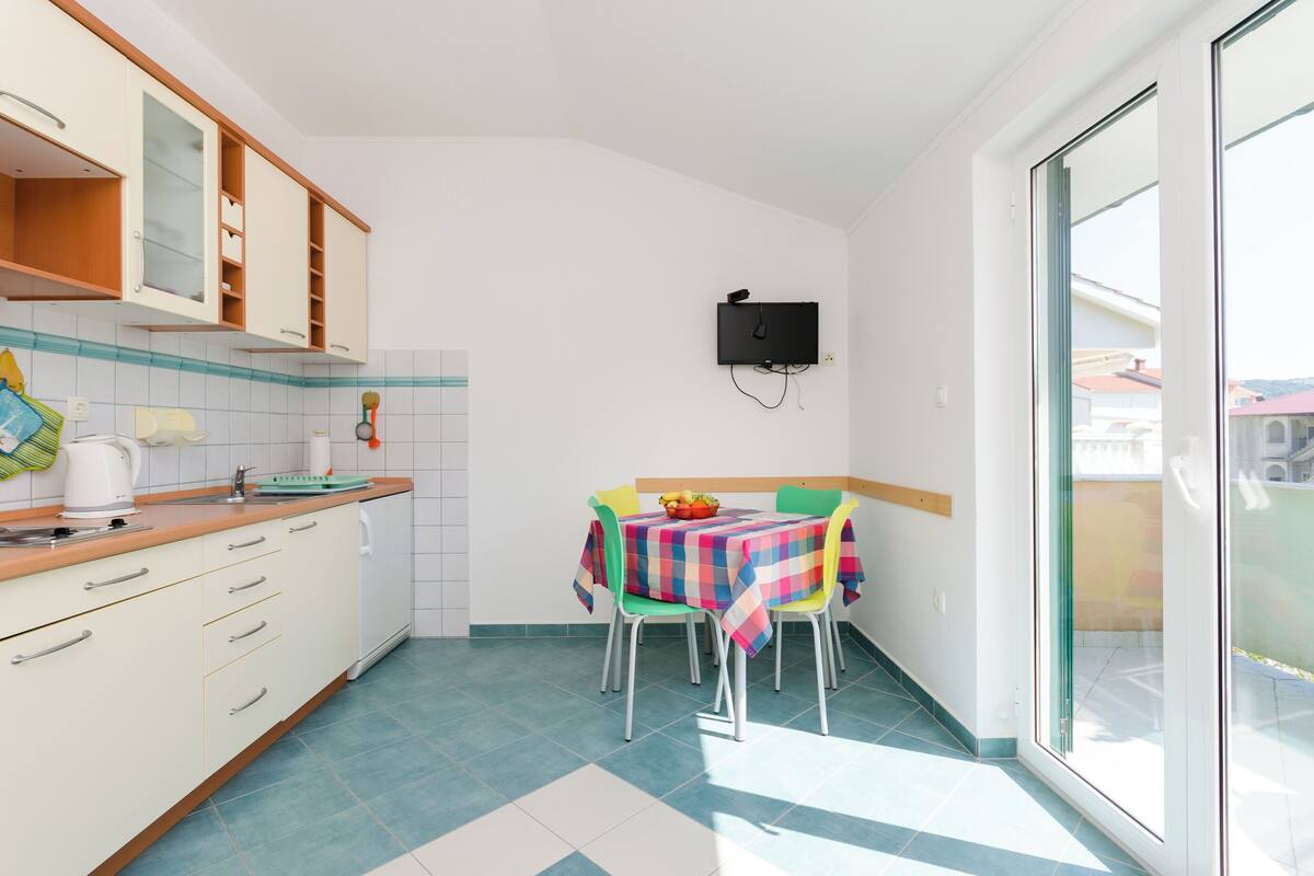 A compact kitchen with a dining area, a television mounted on the wall, and a sliding glass door leading to an outdoor area.
