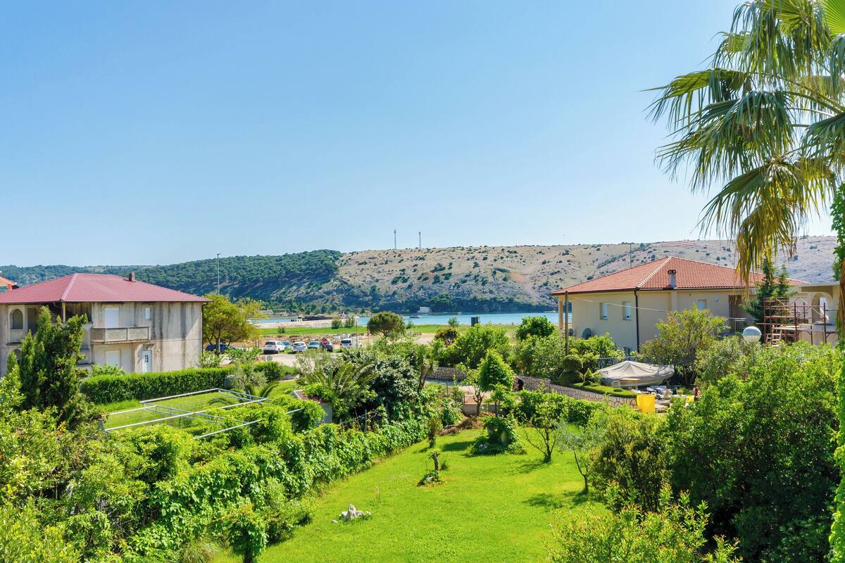 A residential area with houses, a well-maintained garden, and a view of a lake and hills in the background.