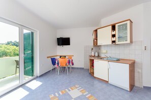 A compact kitchen with a dining area, a television, and a sliding glass door to a balcony. - Apartments Ruzica M (Lopar)