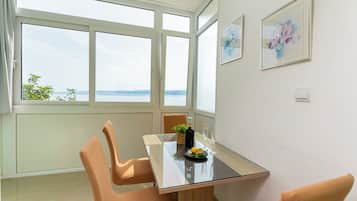 Un comedor con mesa de vidrio, sillas, una planta pequeña y vistas al mar a través de amplios ventanales.