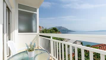 Un balcón con mesa y sillas de vidrio, con vistas a la costa, montañas y el mar.