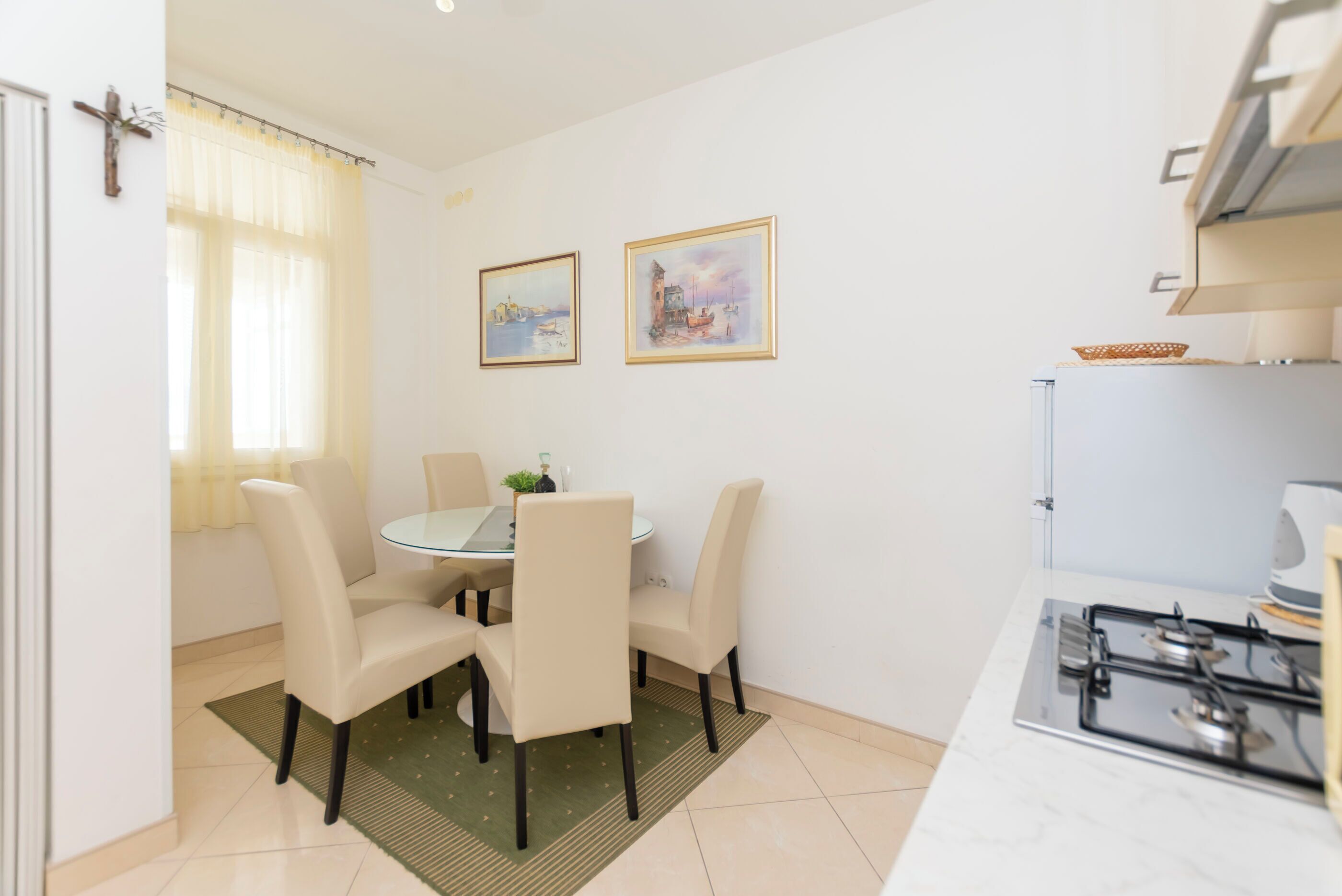 A modern kitchen with a gas stove, a dining table with four chairs, and two framed pictures on the wall.