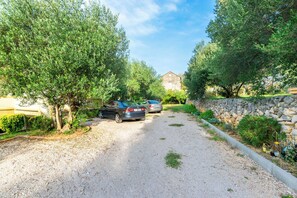 A gravel driveway leading to a stone wall and a building with a sloped roof. - Apartments Sabina (Rab)