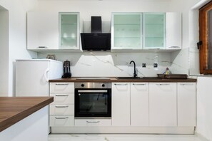 A modern kitchen with white cabinetry, a built-in oven, a microwave, and a sink. - Apartments Sabina (Rab)