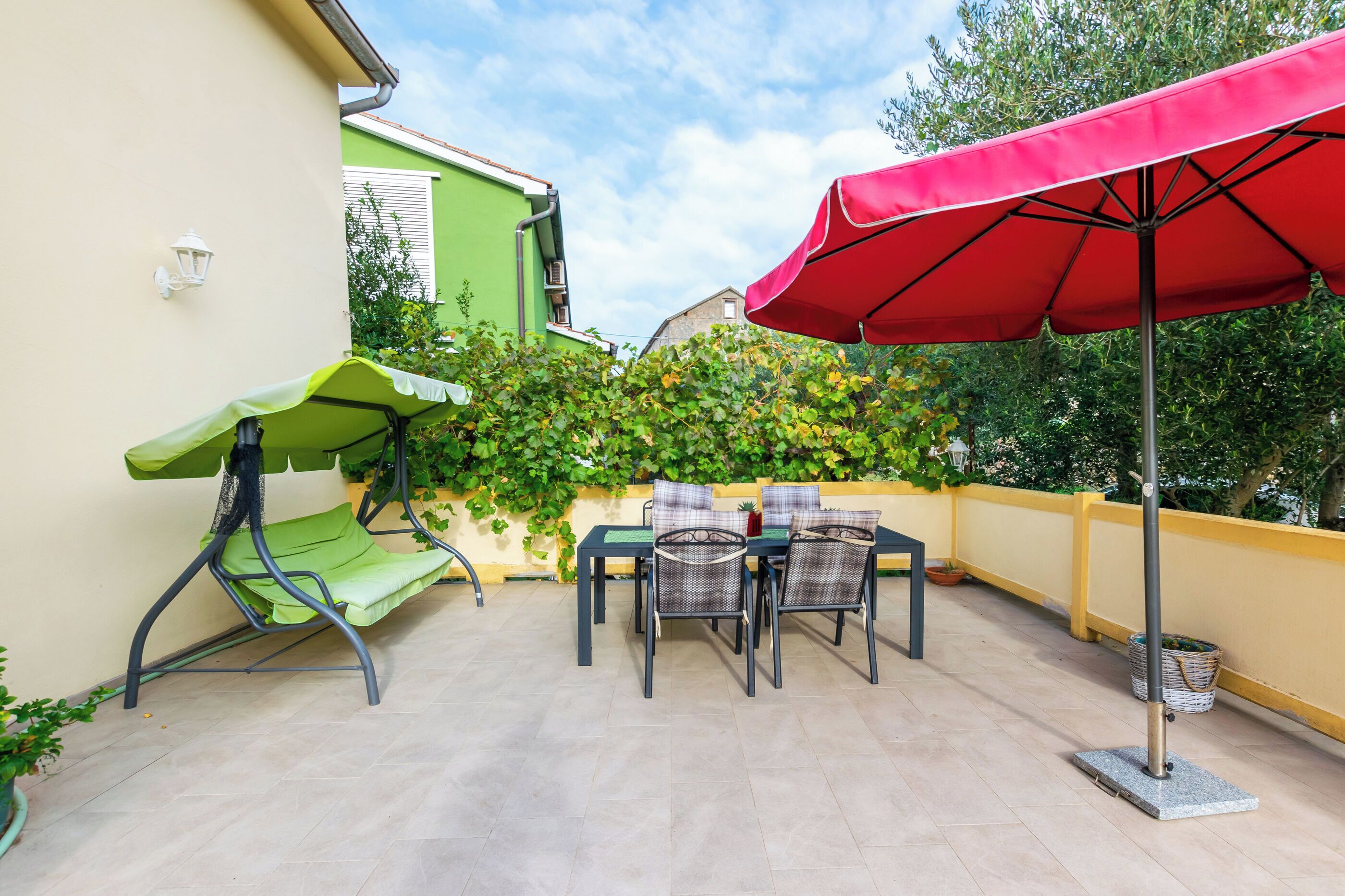 Un patio con tavolo e sedie, un'altalena verde e un ombrellone rosso.