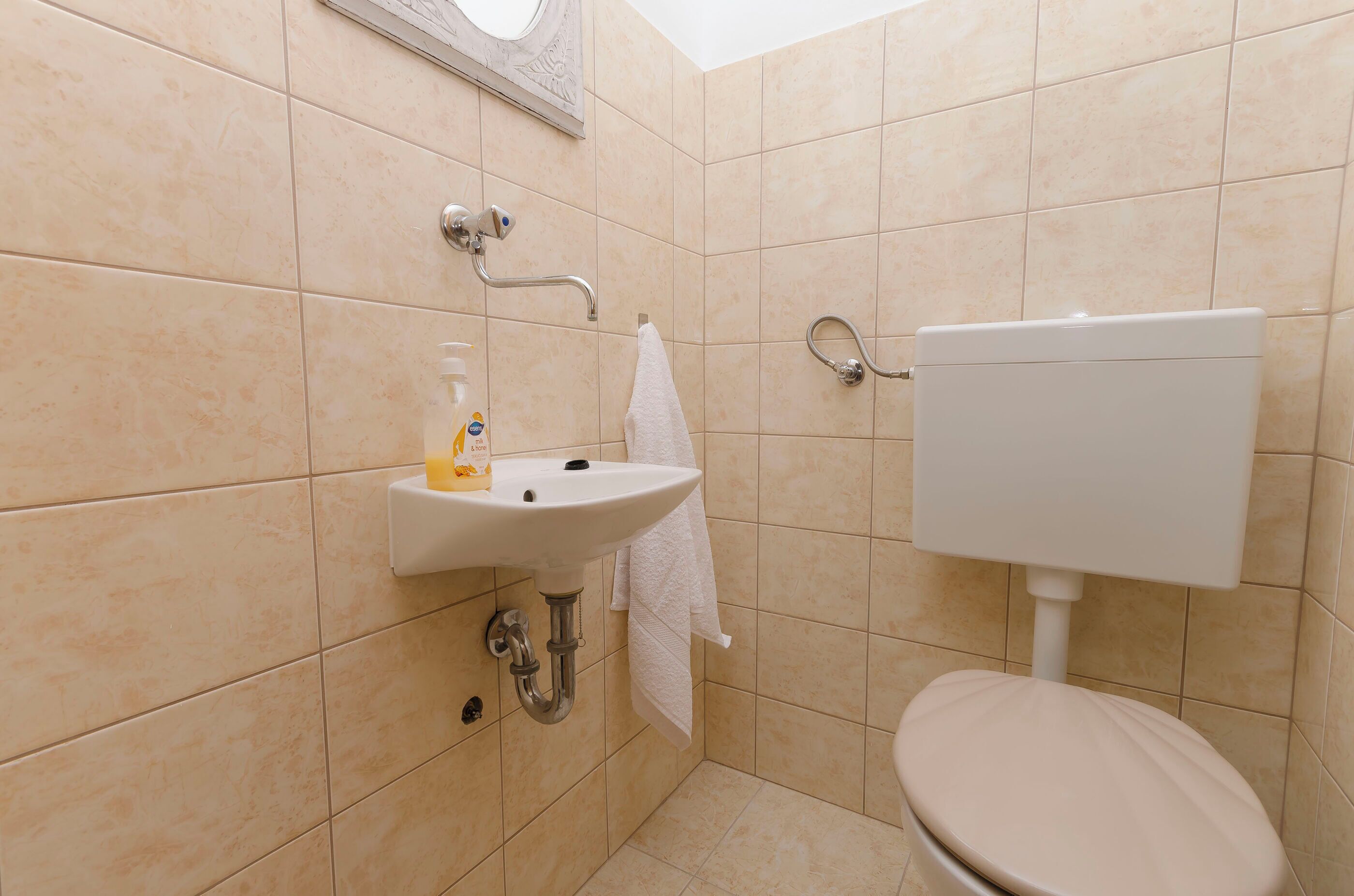 A bathroom with beige tiles, a white sink, a toilet, and a mirror.