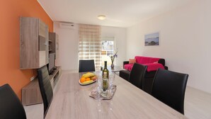 A dining area with a table set for four, a fruit bowl, a bottle of wine, and a vase with flowers. - Apartment Fourstars (Vodice)
