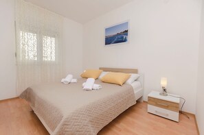 Un lit bien fait, recouvert d’une couette beige, avec deux oreillers et deux serviettes enroulées. On aperçoit une table de chevet avec une lampe et un tiroir.