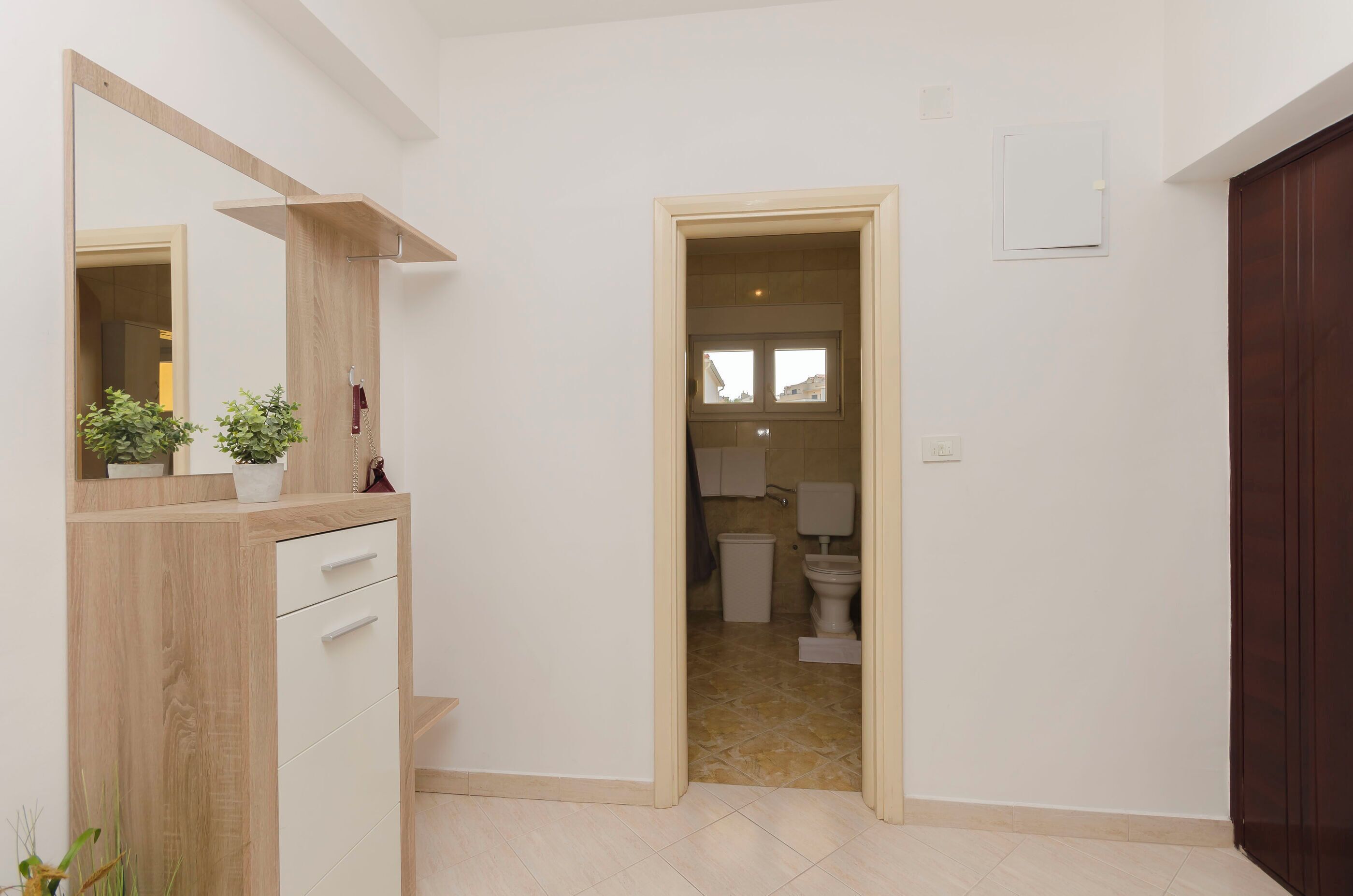 A hallway leading to a bathroom with a toilet and sink. There is a wooden cabinet with drawers and a mirror on the left.