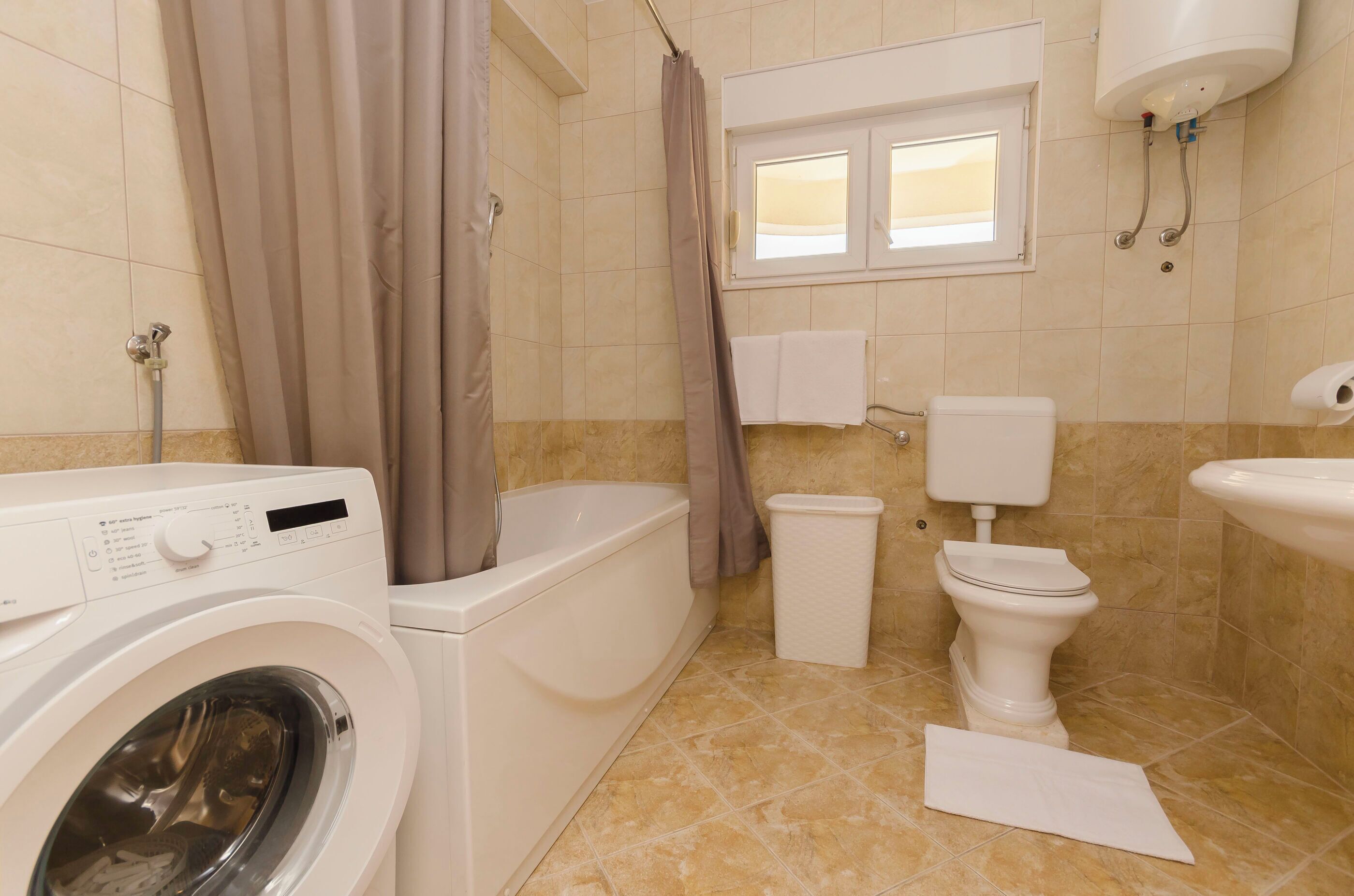A bathroom with a washing machine, a bathtub, a toilet, and a sink.