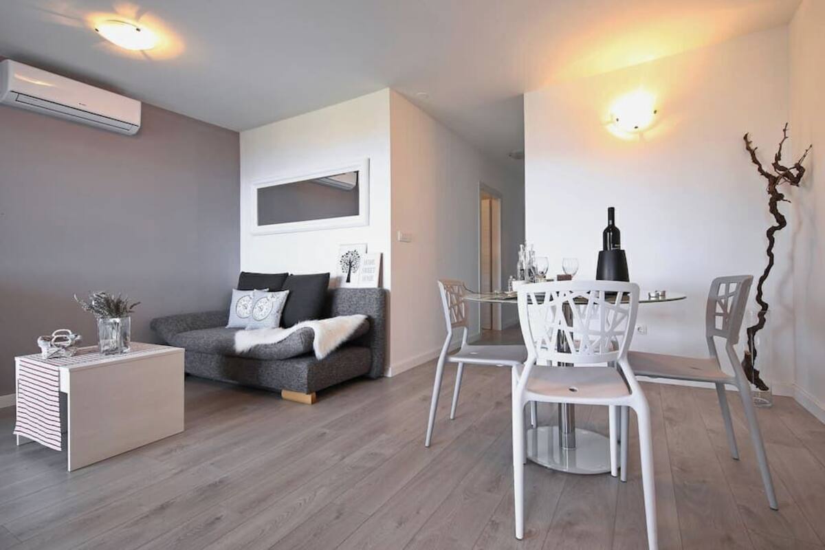 Un salon moderne avec un canapé gris, des chaises blanches et une table à manger.
