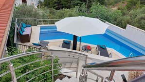 A swimming pool with a white umbrella, lounge chairs, and a staircase leading to a terrace. - Apartment Relax (Omis)