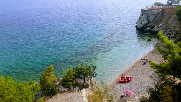 A coastal beach with clear water, rocky terrain, and a red boat on the shore. - Apartment Relax (Omis)