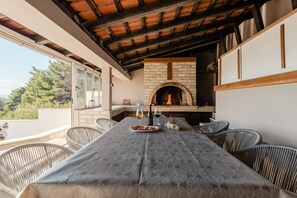 Ein Essbereich im Freien mit Kamin aus Backsteinen, Korbstühlen und einem Tisch für zwei Personen.