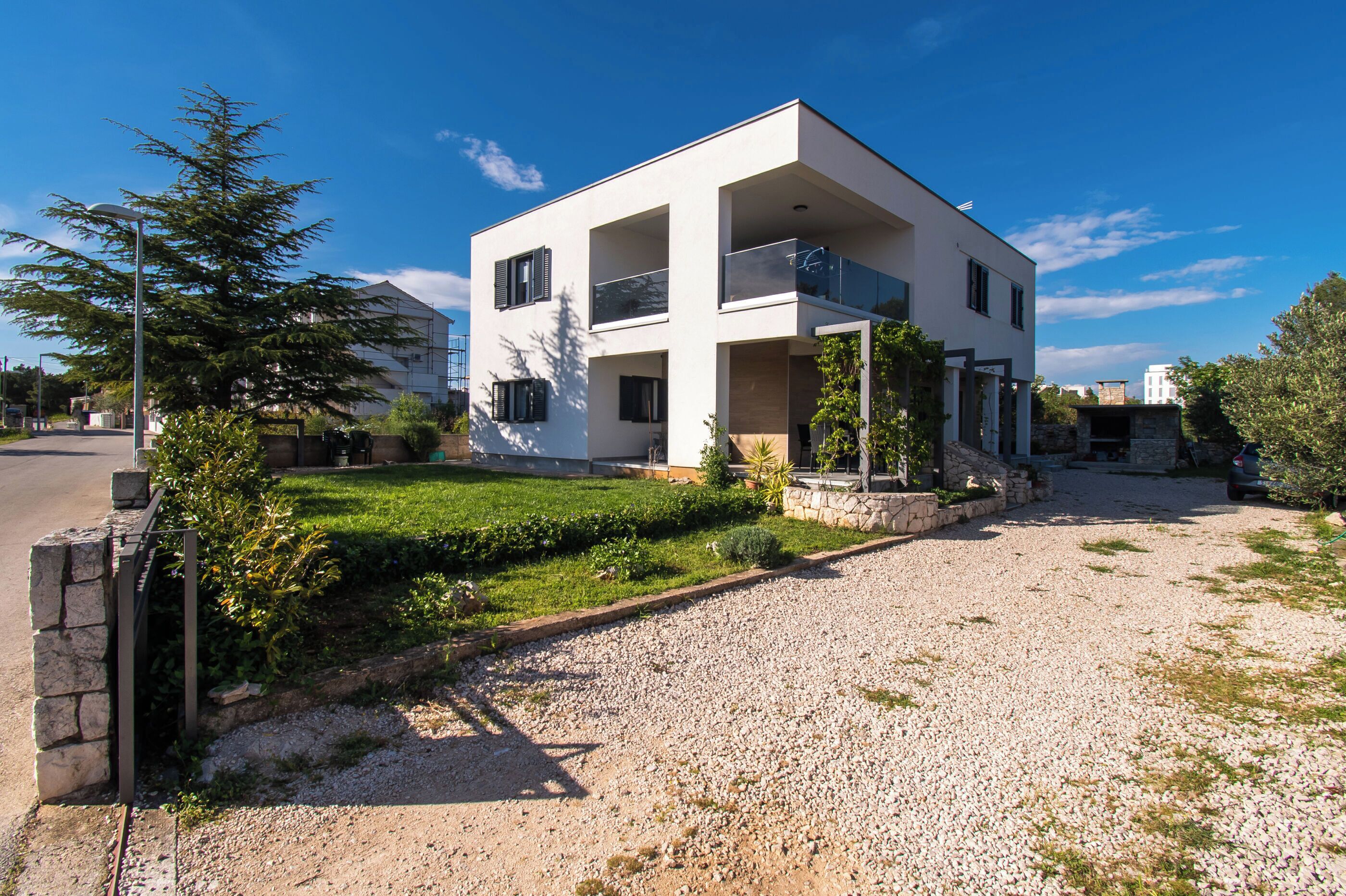 A modern two-story house with a balcony, a gravel driveway, and a well-maintained lawn.