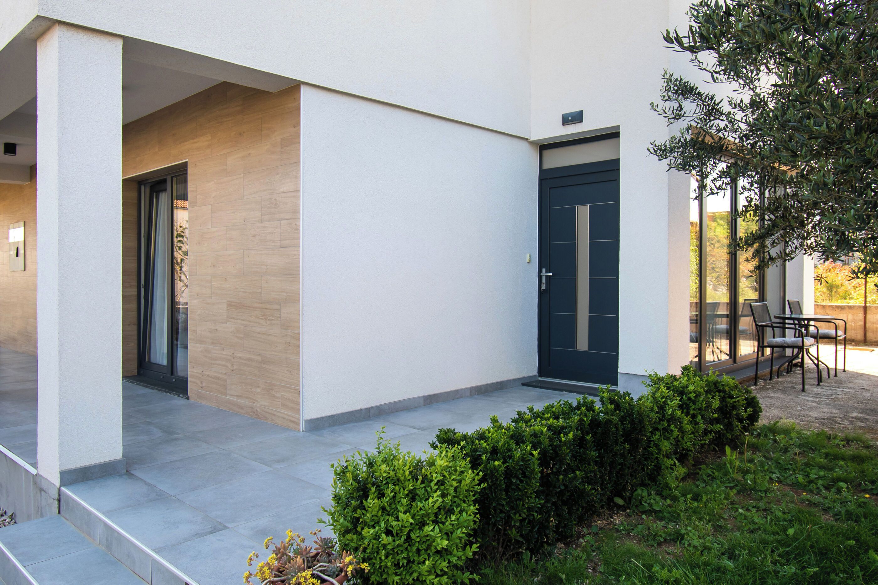 A modern building with a covered entrance, a dark door, and a seating area with chairs and tables.