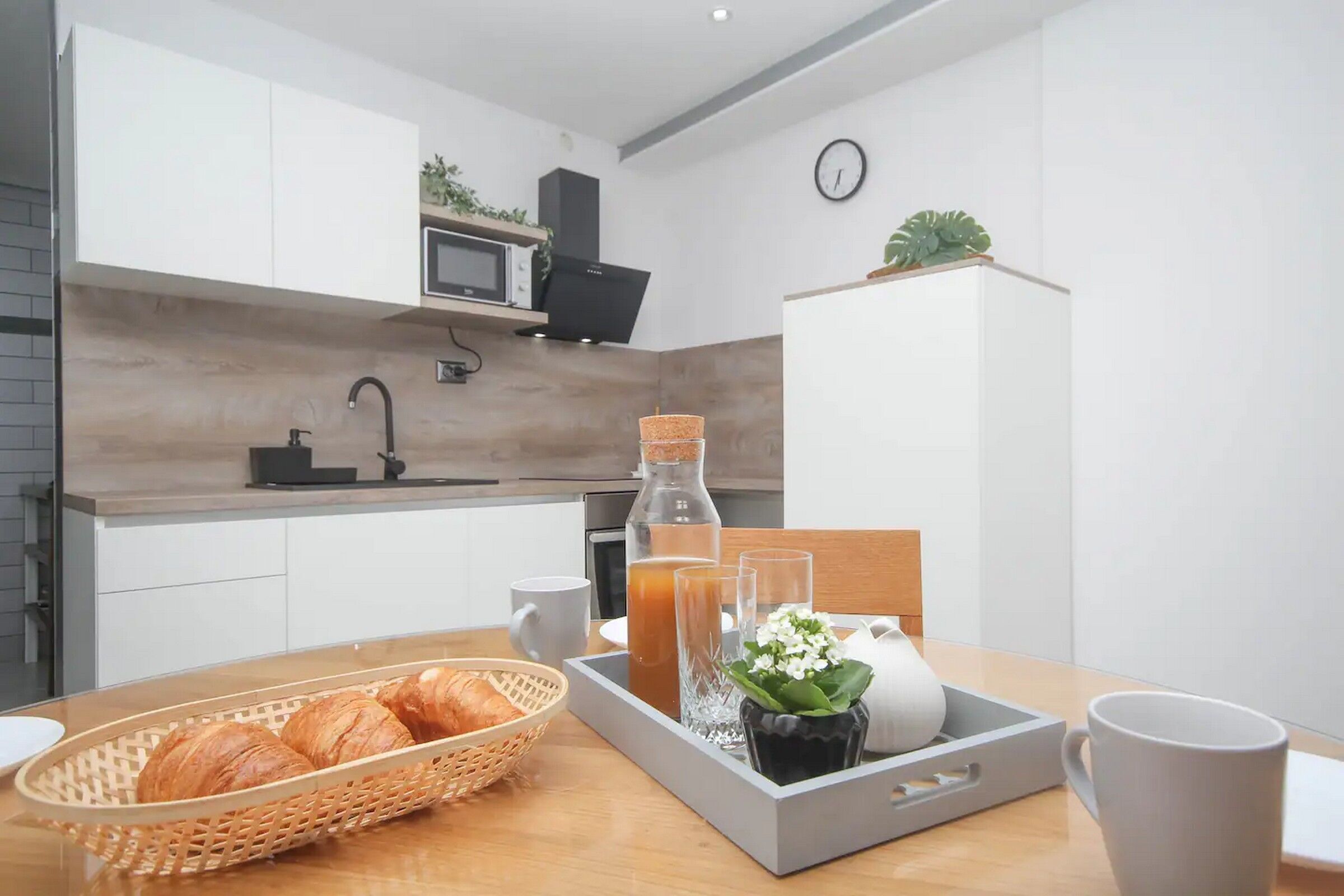 Una cucina moderna con mobili bianchi, un forno a microonde e una macchina da caffè. Un vassoio per la colazione con croissant, un bicchiere di succo e una brocca bianca.