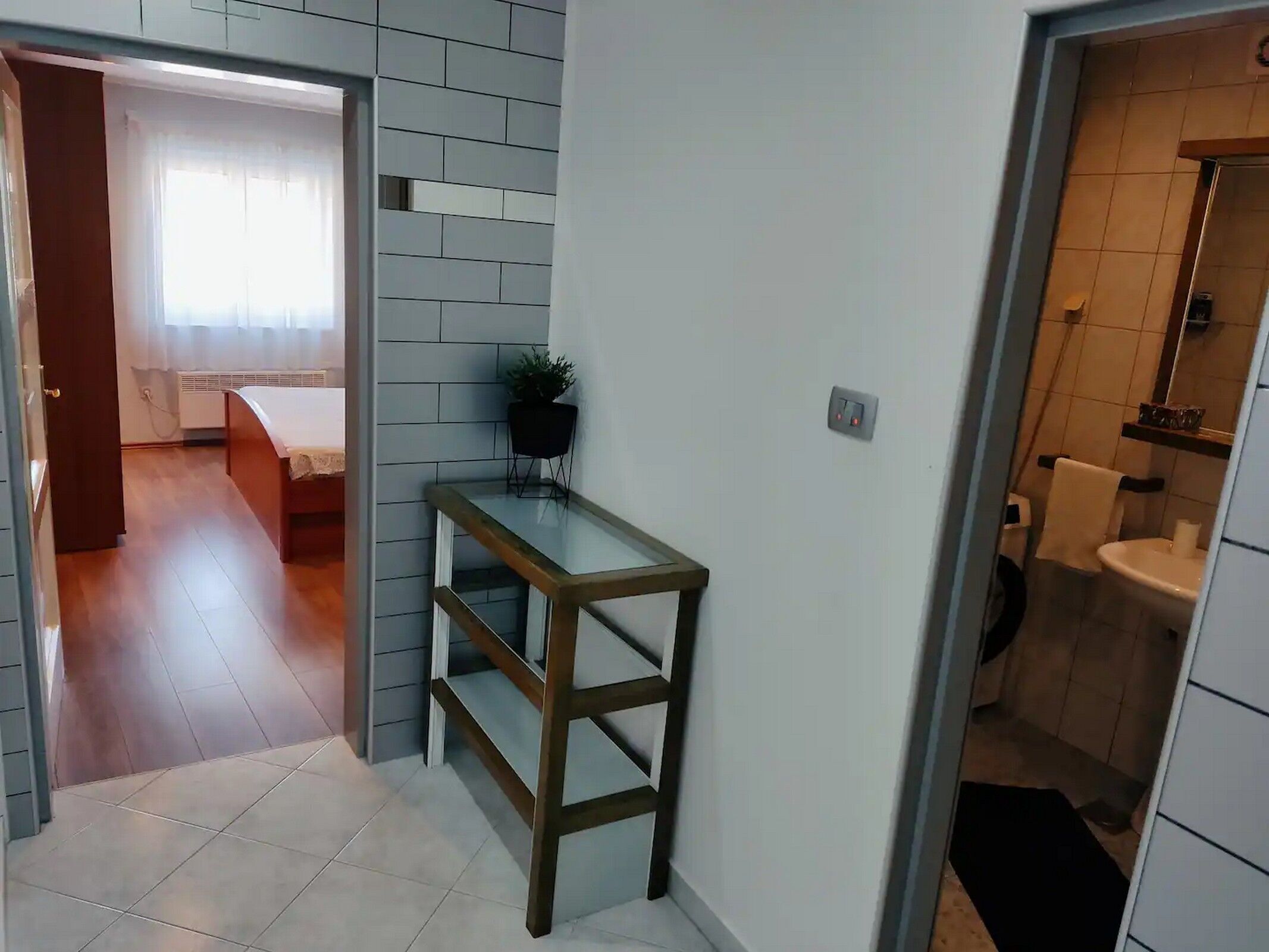 A hallway with a wooden table, a potted plant, and a bathroom with a sink and toilet.
