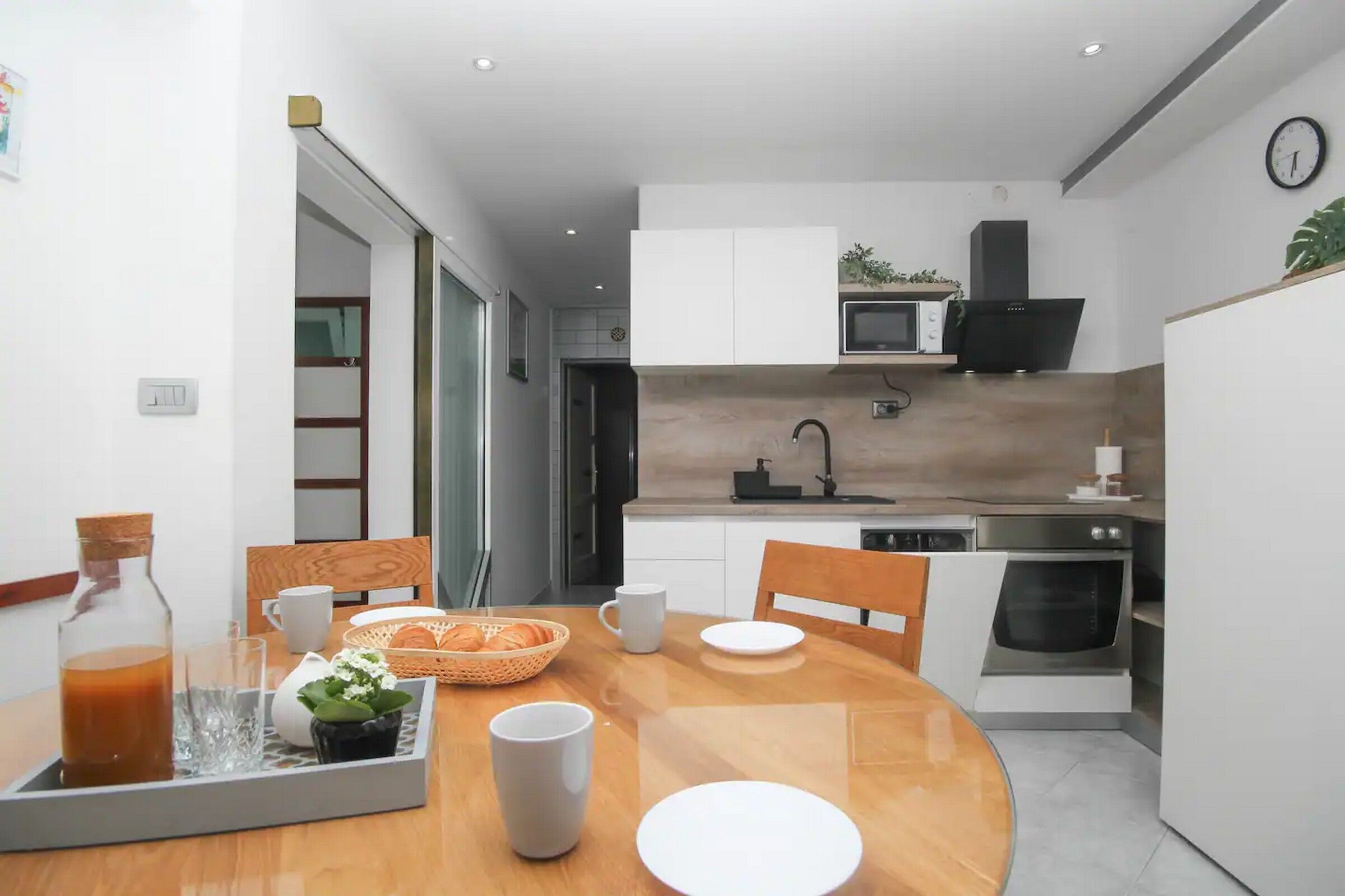 A modern kitchen with white cabinets, a microwave, and an oven. There is a dining table with chairs and a tray with breakfast items.
