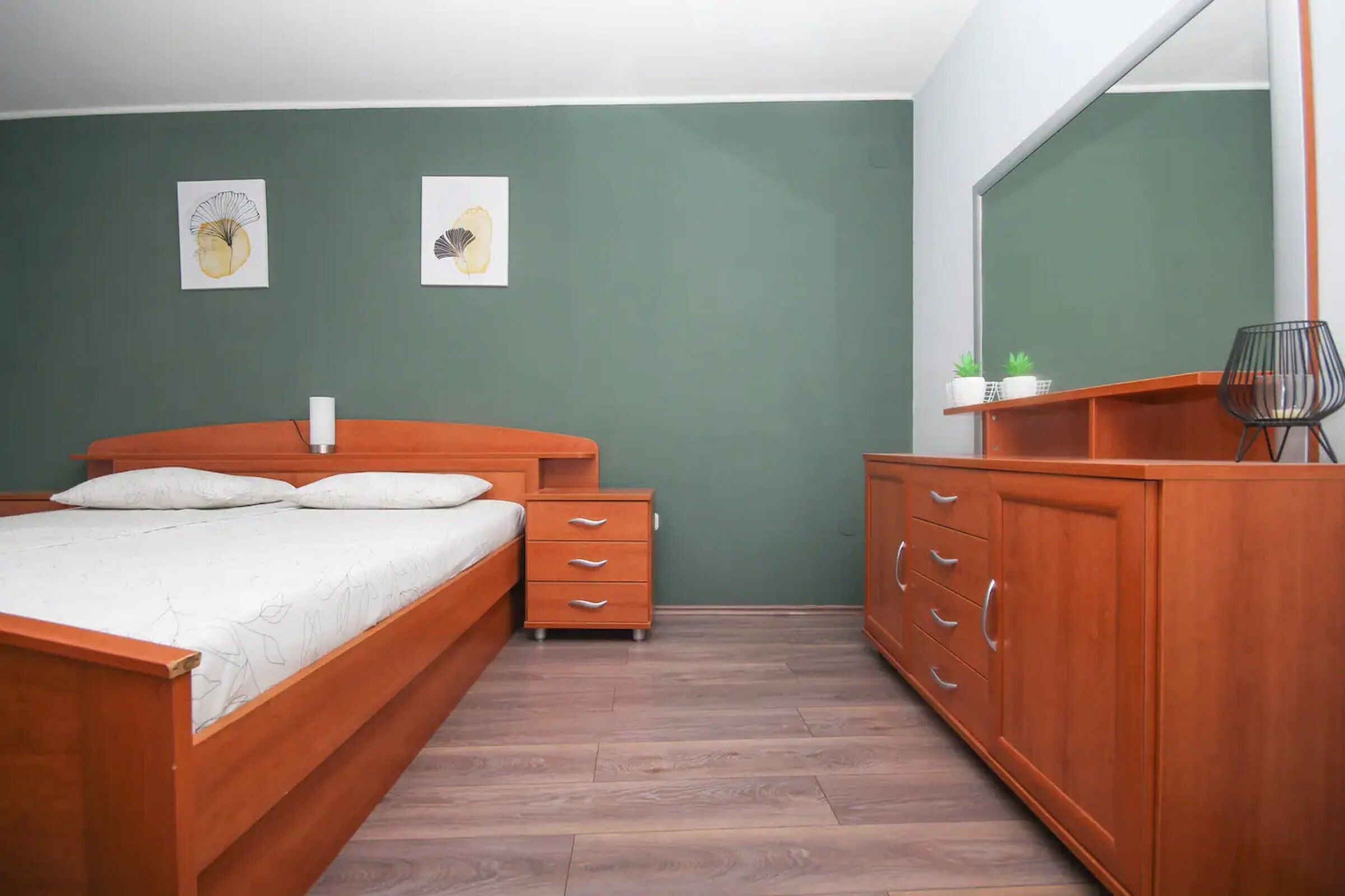 Un dormitorio con una cama de madera, una mesita de noche, un aparador y un espejo.