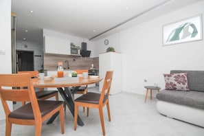 A modern kitchen with white cabinets, a microwave, and a coffee machine. There is a dining table with chairs and a sofa in the living area. - Apartment Toni (Vodice)