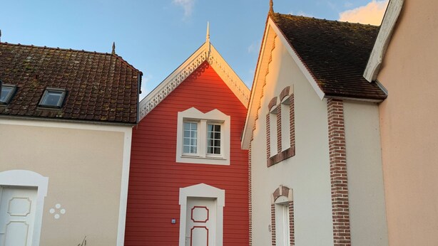 A narrow street with buildings featuring red and white facades, a visible door, and a window. - Charming 3-bedroom house in Belle Dune (Fort-Mahon-Plage)