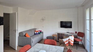A modern living room with a grey sofa, red chairs, a marble coffee table, and a flat-screen TV mounted on the wall. - Charming 3-bedroom house in Belle Dune (Fort-Mahon-Plage)