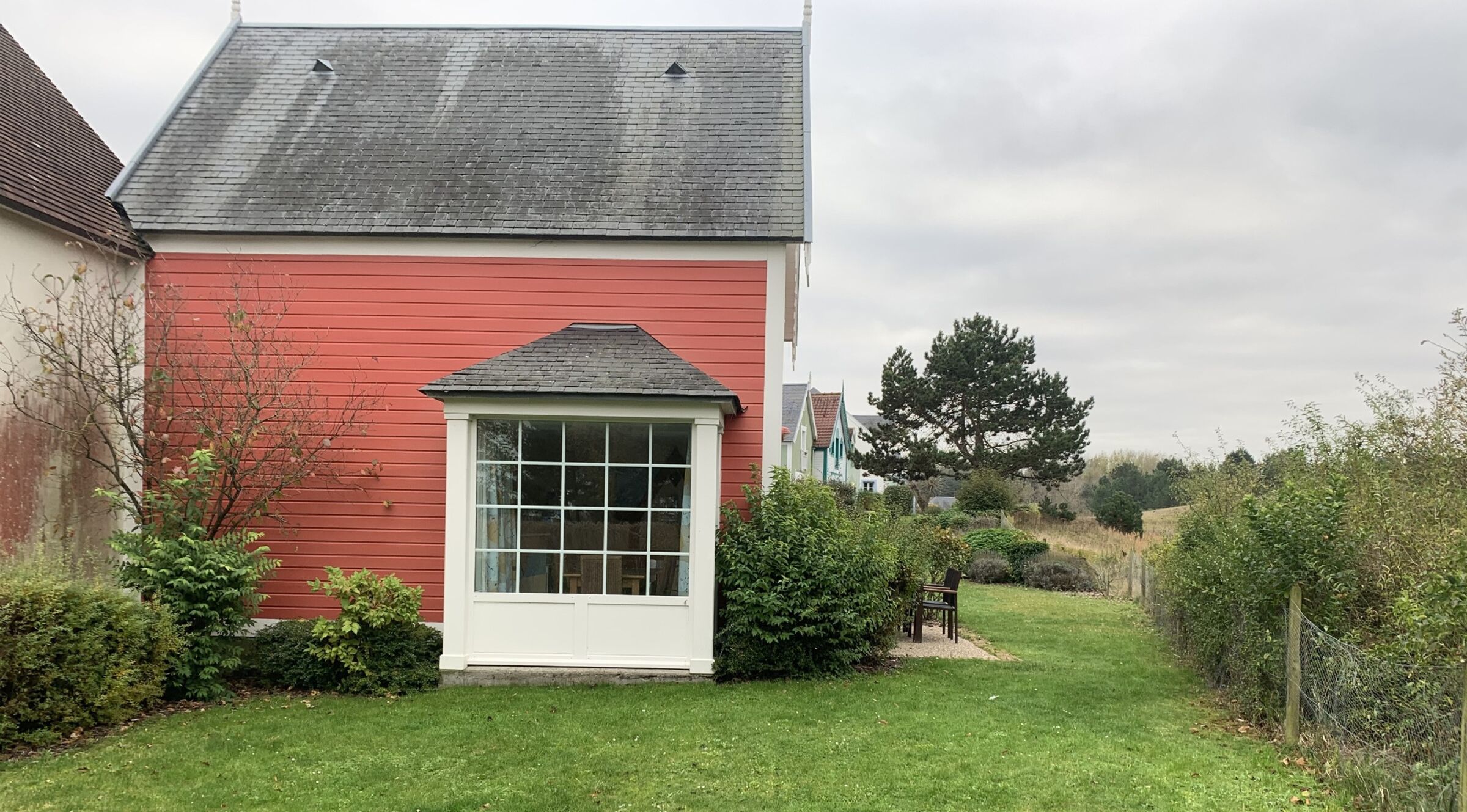 Ein rotes Haus mit weißem Tür- und Fensterrahmen, umgeben von einer kleinen Rasenfläche und Büschen.