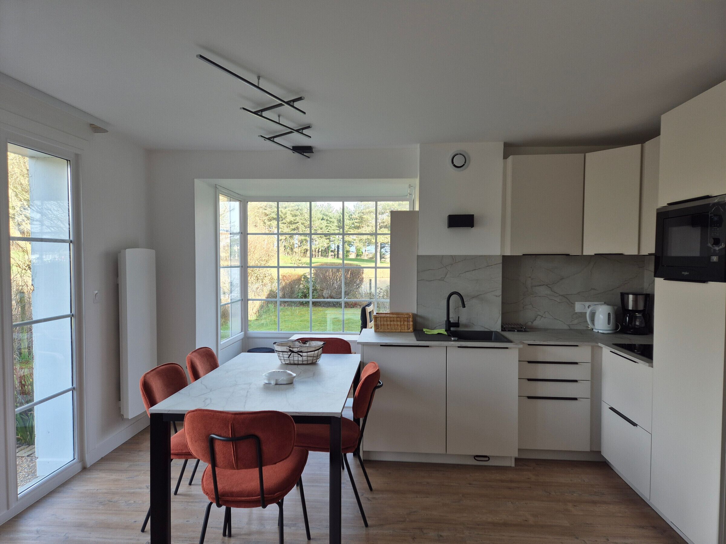A modern kitchen with white cabinets, a large window, and a dining area with a table and chairs.