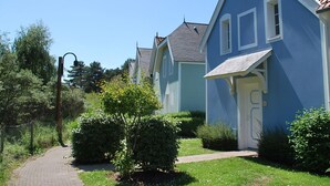A row of blue houses with a paved path leading to the entrance, surrounded by greenery. - Family home in the heart of Domaine Belle Dune (Fort-Mahon-Plage)