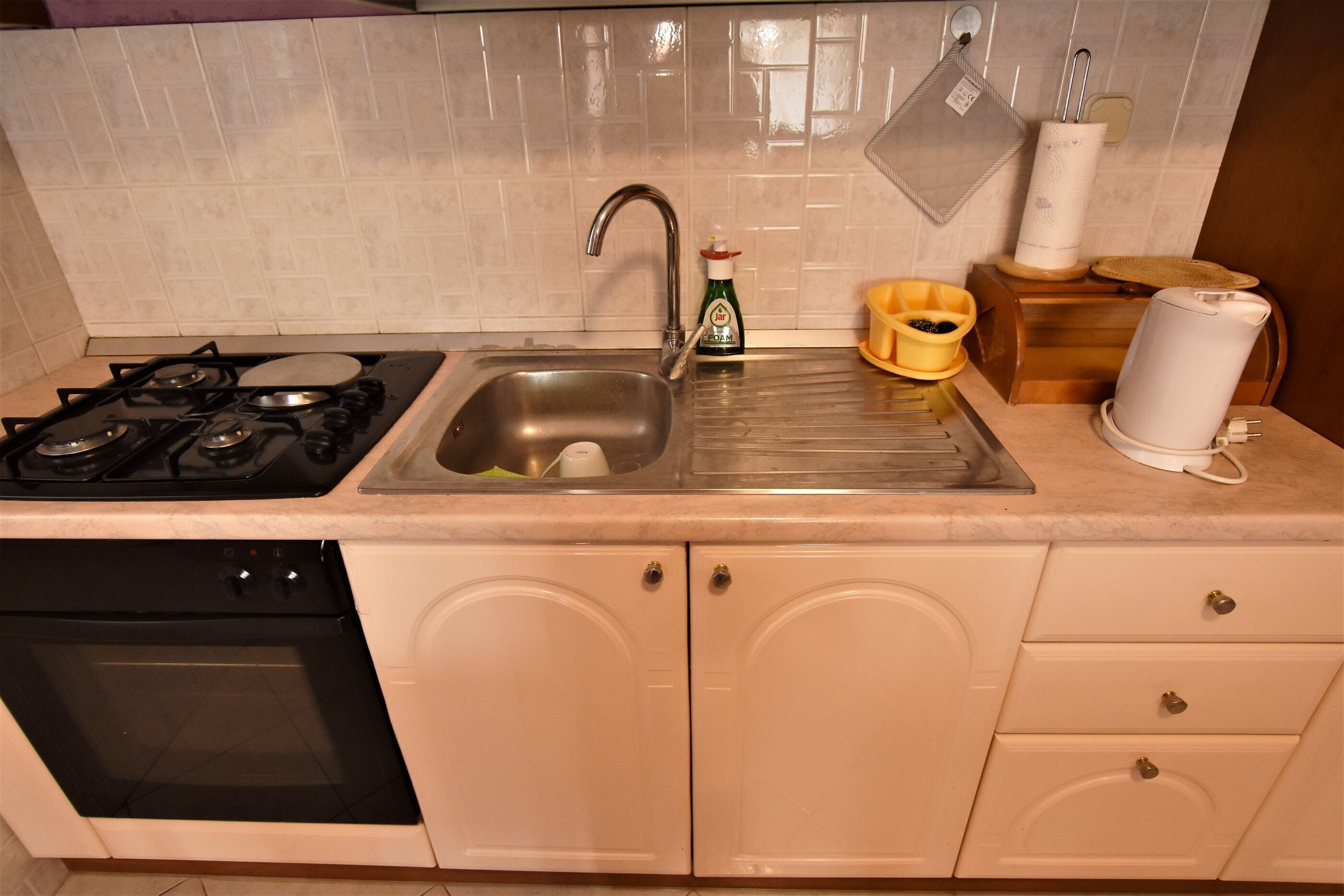 A kitchen with a gas stove, sink, and oven. There is a dish rack, a bottle of dish soap, and a paper towel holder on the countertop.