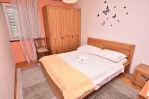A bedroom with a bed, a wardrobe, a nightstand, a chair, and a window with curtains. - Apartment Granum (Biograd na Moru)
