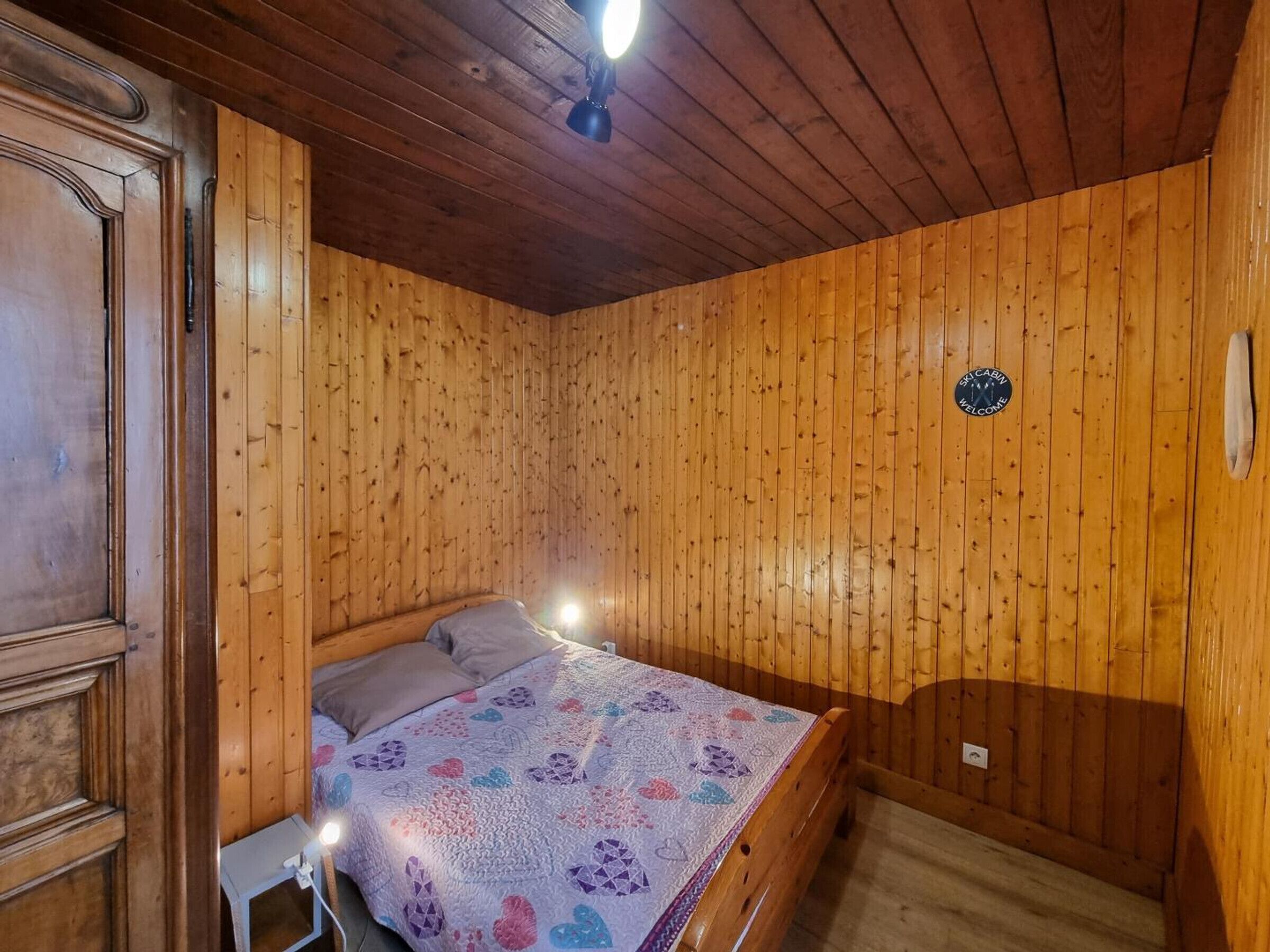 A wooden-paneled room with a bed, a nightstand, and a ceiling light.